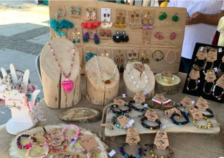 Stoisko z rękodzielniczą biżuterią z naturalnych kamieni na drewnianych ekspozytorach.